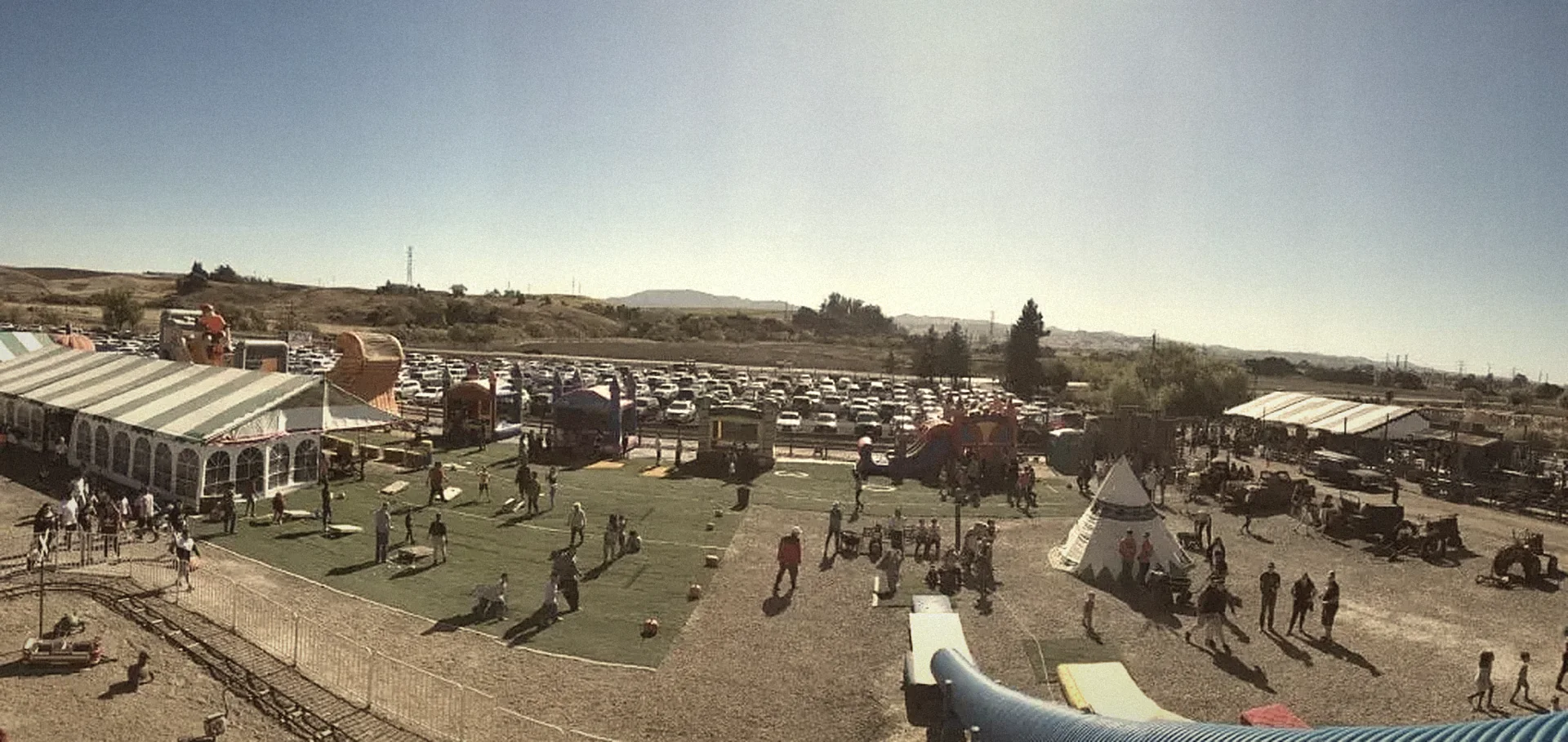 Overhead view of the Pronzini Farms pumpkin patch in Petaluma: families on the green, the big white event tent, inflatable slides, parking rows and the hills beyond